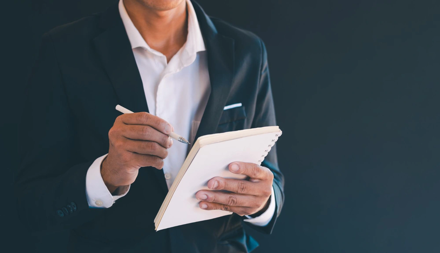 Homem de terno escrevendo em um caderno com caneta, fazendo check list de tarefas para google ads