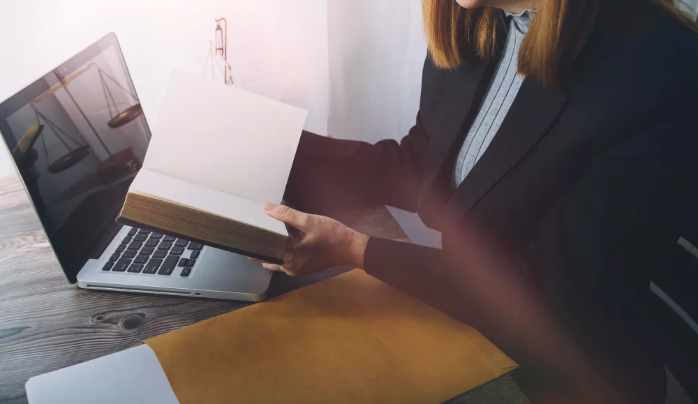 Advogada analisa livro em frente ao laptop com balança da justiça, focando em posicionamento digital para advogados.