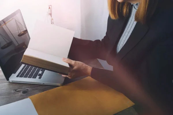 Advogada analisa livro em frente ao laptop com balança da justiça, focando em posicionamento digital para advogados.